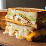 A stacked CHICKEN AVOCADO MELT SANDWICH with melted cheese and toasted bread.
