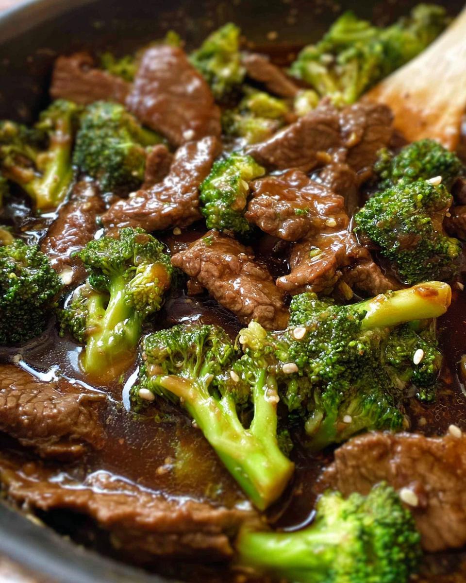 Close-up of tender slices of beef and vibrant broccoli florets coated in a glossy sauce, sprinkled with sesame seeds.
