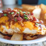 A delicious piece of Cowboy BBQ Bacon Cheddar Chicken topped with melted cheddar cheese, crispy bacon, and chives, served with toasted bread.
