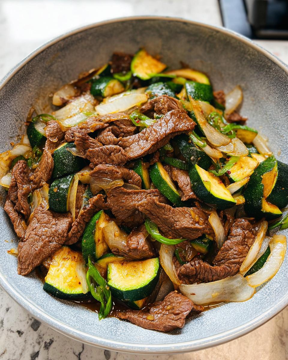 A close-up of a Cozy Grilled Steak Bowl with Zucchini, featuring tender steak slices, zucchini rounds, and onions in a savory sauce.