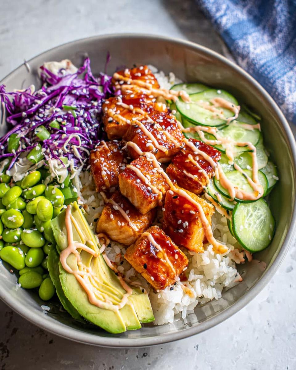 A delicious Crispy Salmon and Rice Bowl topped with sauce, sesame seeds, avocado, cucumber, edamame, and red cabbage.