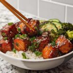 A close-up of a Crispy Salmon and Rice Bowl, with chopsticks picking up a piece of glazed salmon.