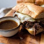 A delicious Crockpot French Dip Sandwich overflowing with shredded beef and melted cheese, served with a side of au jus.