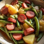 A close-up overhead view of a bowl filled with Crockpot Kielbasa and Green Beans, featuring sliced kielbasa, tender green beans, and chunks of potato.