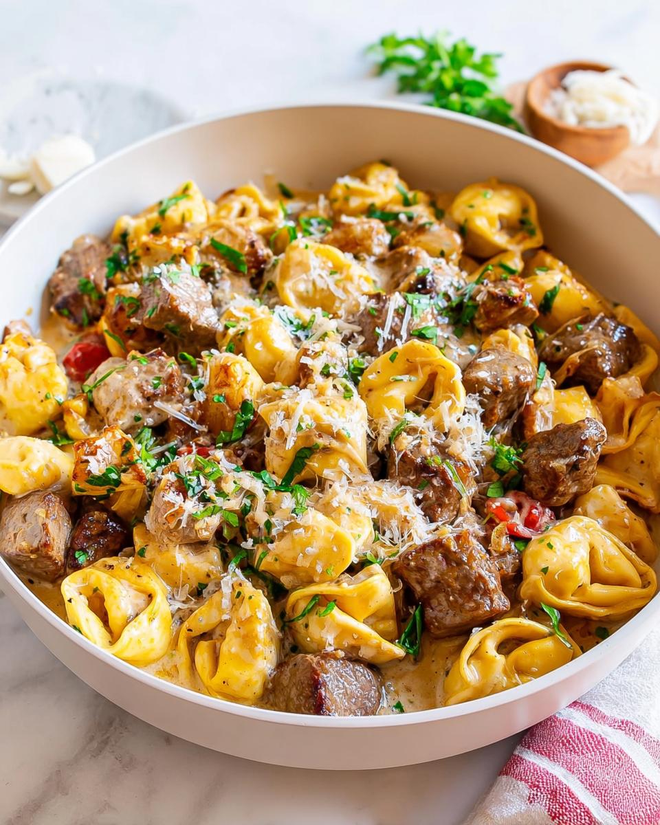 A close-up of a bowl filled with Garlic Steak Tortellini, garnished with parsley and Parmesan cheese.