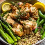 A healthy lemon garlic chicken meal prep bowl with quinoa, asparagus, snap peas, and a creamy sauce.