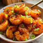 A bowl of High-Protein Honey Garlic Shrimp served over white rice, garnished with green onions and chili flakes.