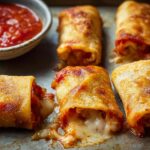 Close-up of golden-brown HIGH PROTEIN Pepperoni Pizza Rolls with gooey melted cheese spilling out, served with marinara sauce.