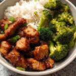 A delicious Honey Garlic Pork Rice Bowl featuring tender pork pieces, fluffy white rice, and vibrant steamed broccoli florets, garnished with green onions.