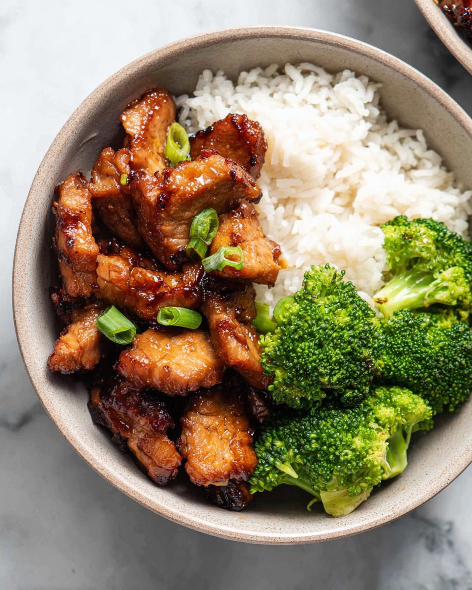 A close-up overhead view of a Honey Garlic Pork Rice Bowl with tender pork, fluffy white rice, and vibrant steamed broccoli florets.