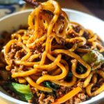 A close-up shot of a bowl filled with Irresistible Yaki Udon Noodles, featuring thick noodles coated in a savory sauce with minced meat and vegetables.