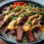 Close-up of Korean BBQ Steak Rice Bowls topped with a creamy, spicy sauce, green onions, and sesame seeds.