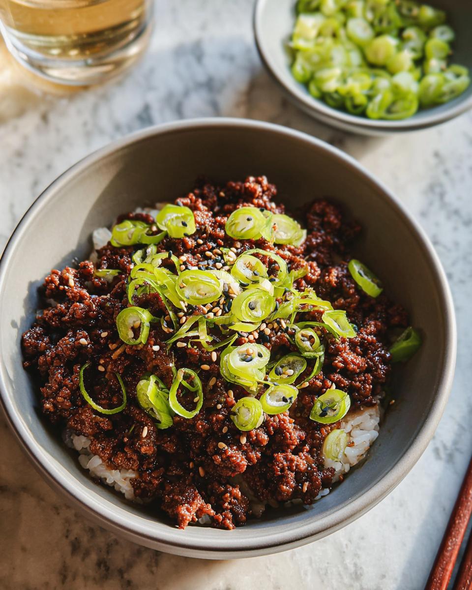A close-up of a Korean Ground Beef Bowl served over white rice, topped with sliced green onions and sesame seeds.