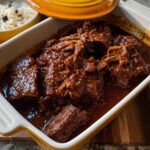 Close-up of a Korean Style Pot Roast, with tender, shredded beef in a rich, dark sauce, served in a baking dish.