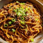 A close-up shot of a bowl filled with Mongolian Ground Beef Noodles, garnished with sesame seeds and chopped green onions.