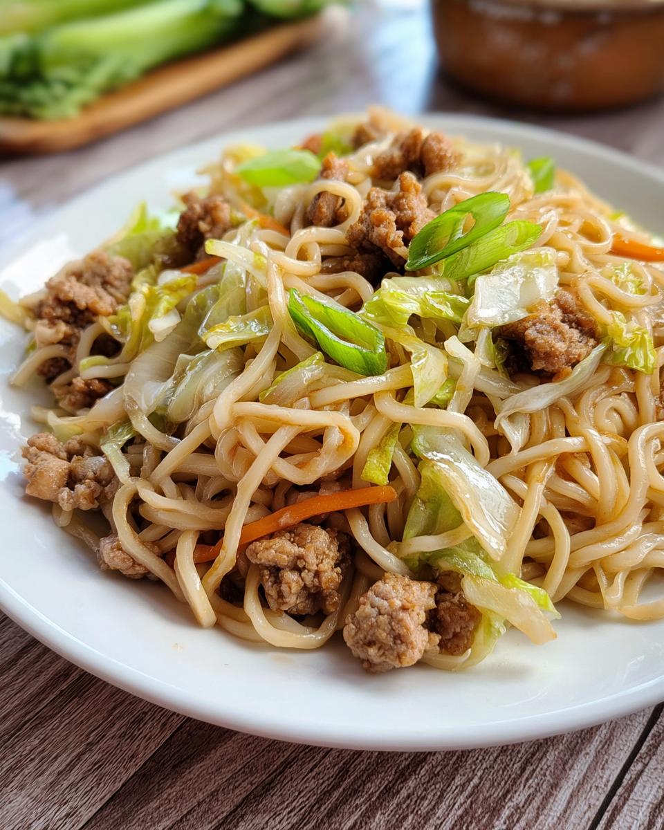 A close-up of a Potsticker Noodle Bowl with savory pork, tender noodles, and fresh cabbage slaw, garnished with green onions.