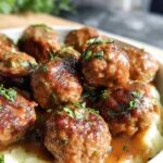 Close-up of Salisbury steak meatballs smothered in gravy, served over fluffy garlic herb mashed potatoes and garnished with parsley.