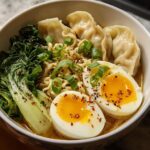 A close-up of a Savory Dumpling Ramen Bowl with soft-boiled eggs, dumplings, noodles, and bok choy.
