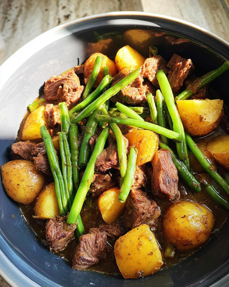 Close-up of Slow Cooker Garlic Butter Beef with Potatoes and tender green beans in a dark bowl.