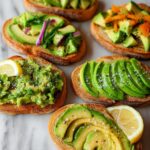 A variety of delicious avocado toast toppings on toasted bread, including sliced avocado, mashed avocado, and red onion.