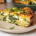 A slice of baked cottage cheese eggs with spinach and feta cheese, topped with green onions.