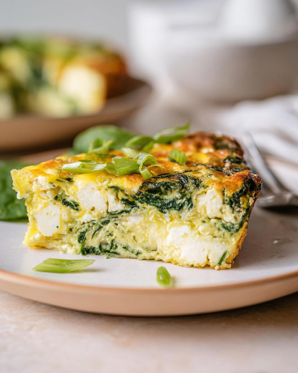 A slice of baked cottage cheese eggs with spinach and feta cheese, garnished with green onions.
