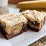 Two slices of Banana Bread Brownies Made Easy, topped with cream cheese frosting and cinnamon.
