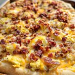 Close-up of a freshly baked breakfast pizza egg recipe topped with scrambled eggs, cheese, and bacon.