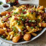 A delicious plate of Breakfast Poutine with Hollandaise Sauce, featuring crispy tater tots, french fries, bacon, and green onions.