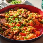A close-up of a skillet filled with Cajun Sausage and Rice, garnished with green onions and bell peppers.