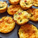 Golden brown Cheesy Muffin Tin Cottage Cheese Egg Bites baked in a muffin tin, with visible bits of bacon and herbs.