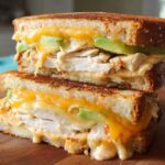 A stacked Chicken Avocado Melt Sandwich with melted cheese, sliced chicken, and avocado on toasted bread.