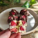 A hand holds a broken Chocolate Strawberry Yogurt Cluster, revealing creamy yogurt and strawberry pieces inside.
