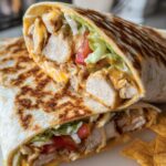 Close-up of an Easy Chipotle Ranch Grilled Chicken Burrito cut in half, revealing seasoned chicken, cheese, lettuce, and tomato.