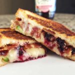 A gourmet blueberry grilled cheese sandwich cut in half, showing melted cheese, blueberries, and bacon.