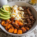 A close-up of a Ground Beef Hot Honey Bowl featuring seasoned ground beef, scrambled eggs drizzled with honey, sliced avocado, and roasted sweet potato cubes.