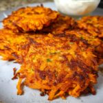 Crispy, golden-brown Healthy Sweet Potato Hash Browns piled on a grey plate, with a small bowl of dip in the background.