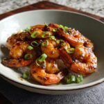A bowl of white rice topped with glistening High-Protein Honey Garlic Shrimp and chopped green onions.