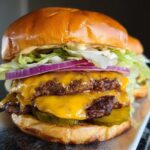 Close-up of a double patty smash burger with melted cheese, pickles, red onion, lettuce, and secret sauce.