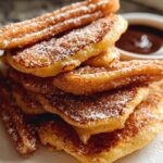 A stack of Irresistible Spanish Churro Pancakes dusted with powdered sugar and cinnamon, served with chocolate dipping sauce.