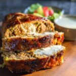 Close-up of sliced Juicy Garlic Parmesan Chicken Meatloaf, drizzled with sauce, with a side of salad.