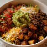 A delicious Loaded Potato Taco Bowl filled with seasoned ground beef, crispy potatoes, pico de gallo, guacamole, and shredded cheese.