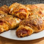 A plate of golden-brown mozzarella pepperoni croissant rolls, sprinkled with herbs.