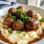 A close-up of Salisbury steak meatballs served over creamy garlic herb mashed potatoes, garnished with fresh parsley.