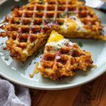 A slice of savory hashbrown chaffle topped with a fried egg, red onion, and parsley.