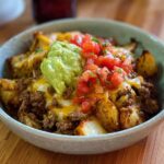A bowl of Schnelle Kartoffel Taco Bowl Meal Prep with seasoned potatoes, ground beef, melted cheese, guacamole, and pico de gallo.