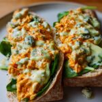 Two halves of a sandwich filled with spicy buffalo chicken, blue cheese, and spinach.