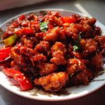 A plate of Spicy Dragon Chicken, featuring crispy fried chicken pieces coated in a glossy, spicy sauce with red peppers and sesame seeds.