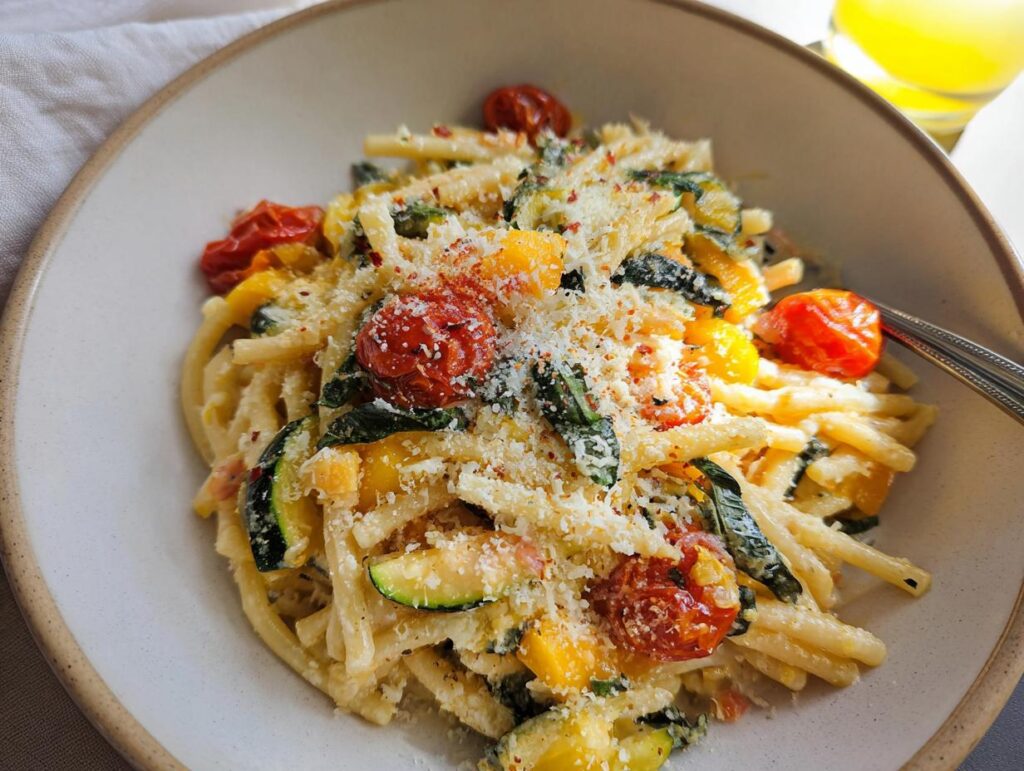 A close-up of a bowl of Tomato Zucchini Pasta, featuring pasta, cherry tomatoes, zucchini slices, and grated cheese.