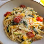 A close-up of a bowl of Tomato Zucchini Pasta, featuring pasta, cherry tomatoes, zucchini slices, and grated cheese.